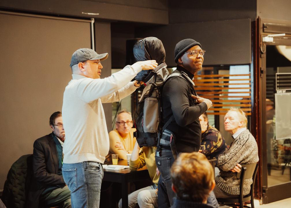 A lecture by two men, one with a rucksack on his back