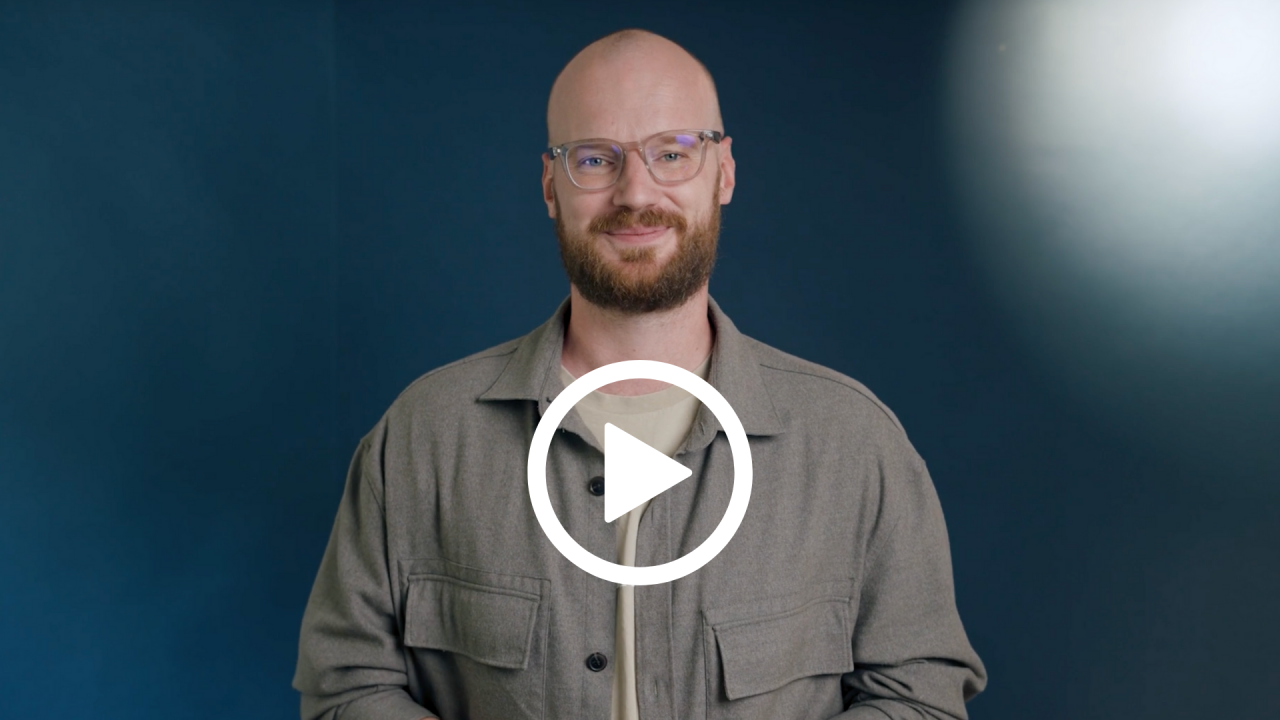 Pastor Jonzi lächelt in die Kamera, auf dem Bild ist ein Playbutton.